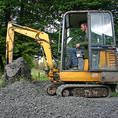 Man i minigrävare gräver i trädgård
