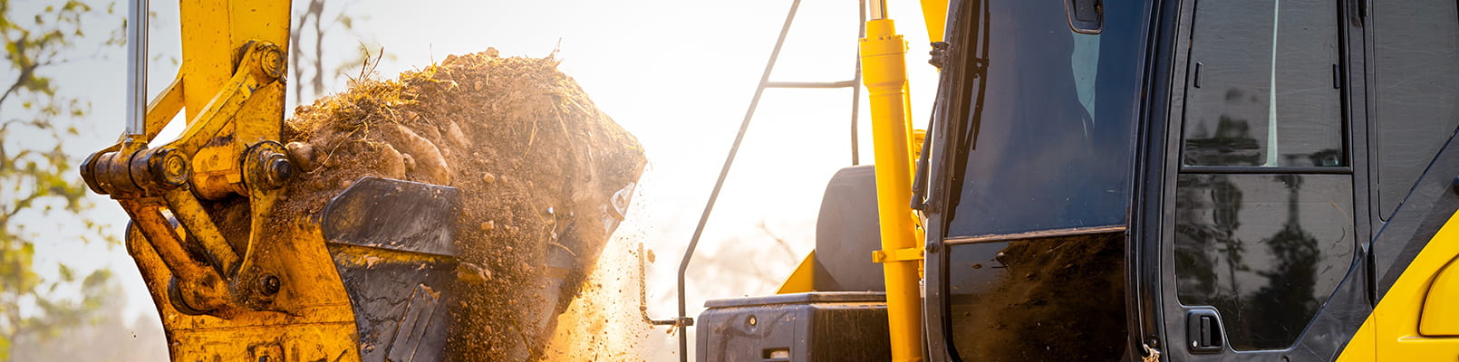 Actionbild på grävmaskin med grävskopa i motljus.