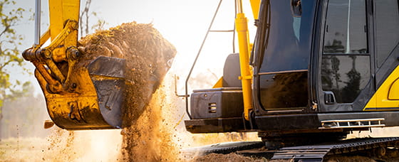 Actionbild på grävmaskin med grävskopa i motljus.