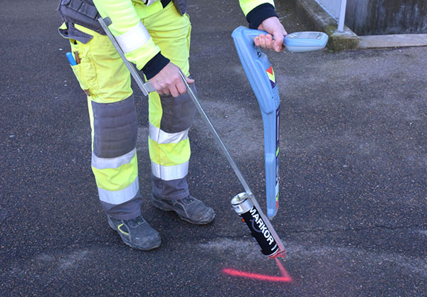 Underkroppen på en person i varselkläder sprayar färg på asfalt.